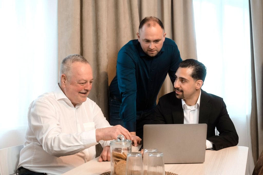 Peter Mennel, Thomas Nadolski und Firat Cagli vom Team der maxXe Versicherungsmakler Nürnberg sprechen miteinander am Besprechungstisch.