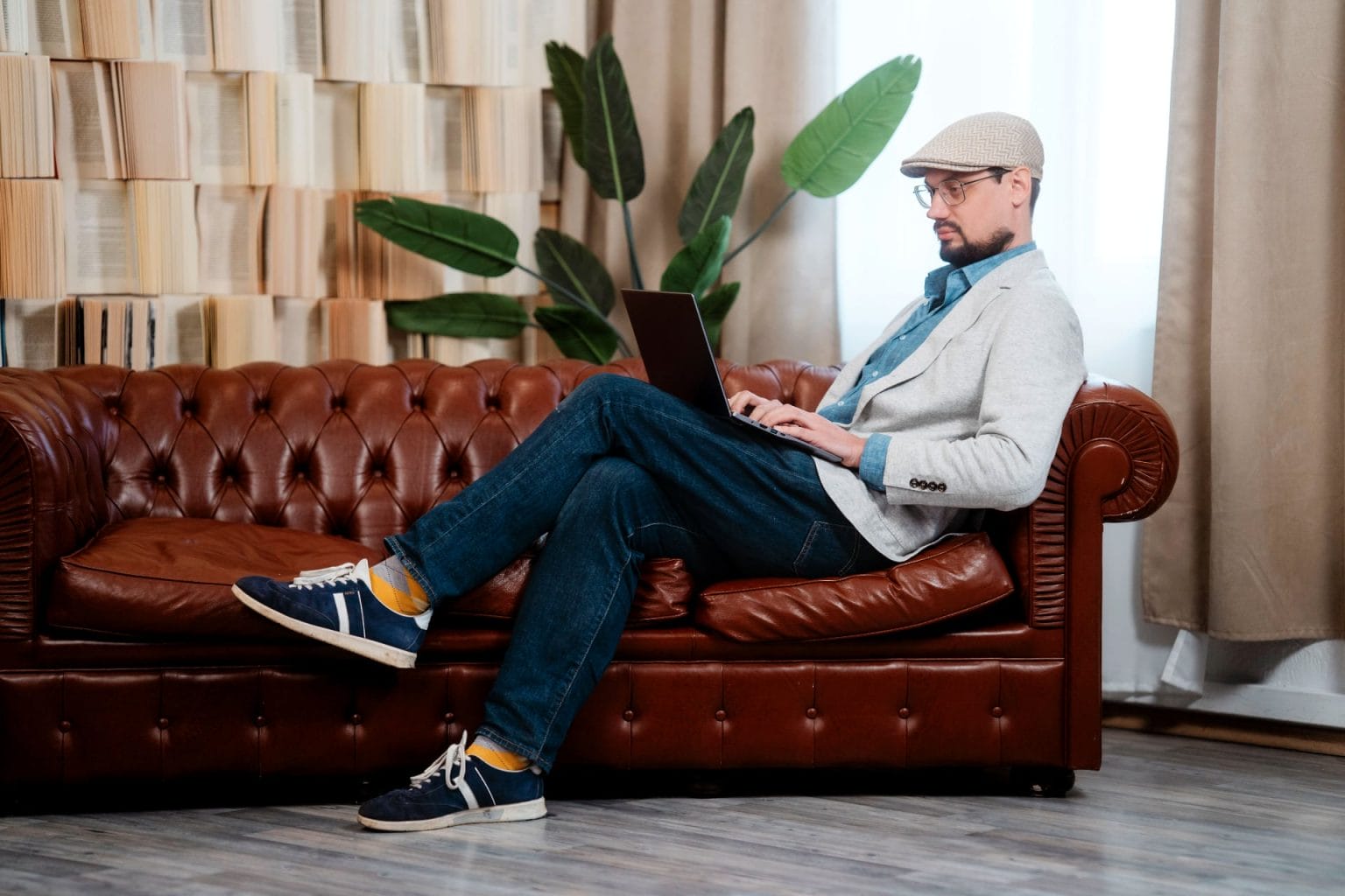 Daniel Preiss sitzt auf einer Couch und arbeitet am Notebook in einem modernen Raum.