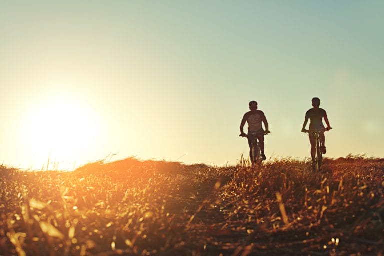 Ein Pärchen fährt bei sonnigem Wetter Fahrrad in der Landschaft. Symbolisch für eine Fahrradversicherung.