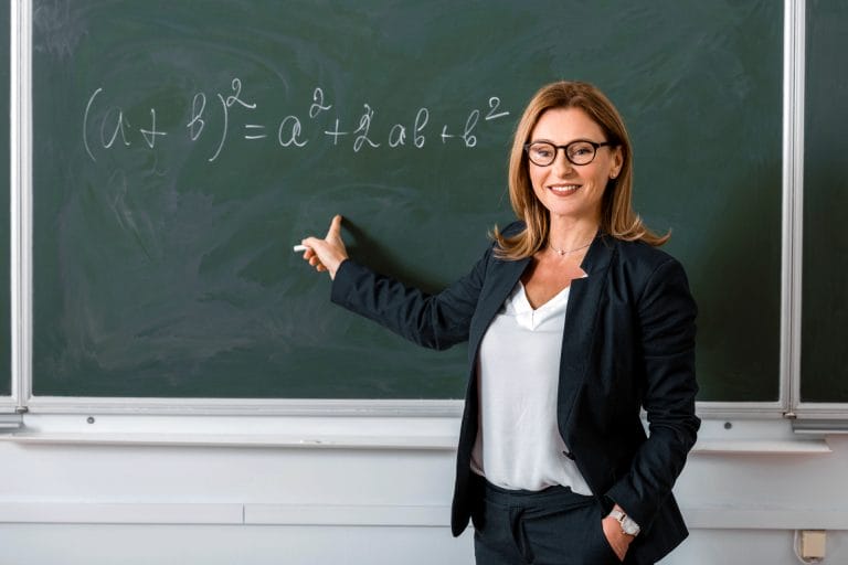 Eine Lehrerin hält Unterricht an der Tafel. Symbolisiert eine private Krankenversicherung für Beamte.