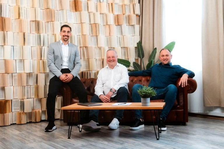 Peter Mennel, Thomas Nodolski und Firat Cagli vom maxXse Team sitzen auf der Couch in einem kreativ dekorierten Zimmer.